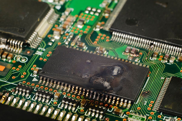Photo of an IC on a PC internal circuit board that has been burned due to electrostatic discharge (ESD). The top surface of the IC is burnt and whitened, and part of the leads and the printed circuit board are burnt and blackened.